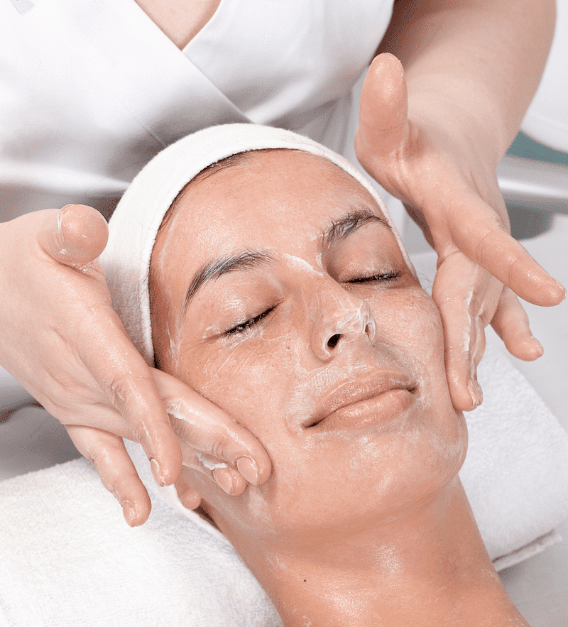Person receiving a relaxing facial treatment, eyes closed and face covered in a white cream.